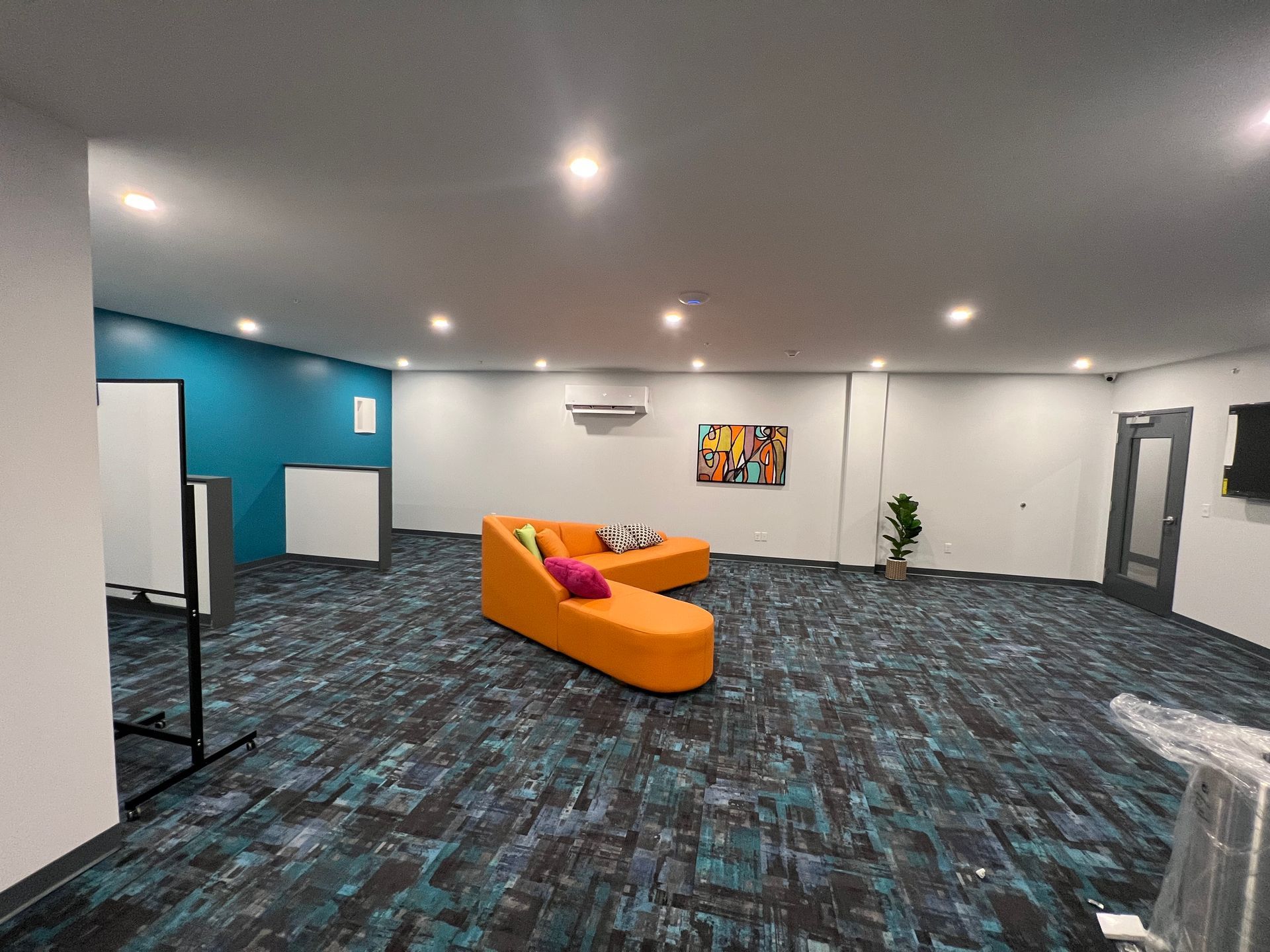 Open office space with blue and orange accents, including a curved orange couch on a patterned carpet.
