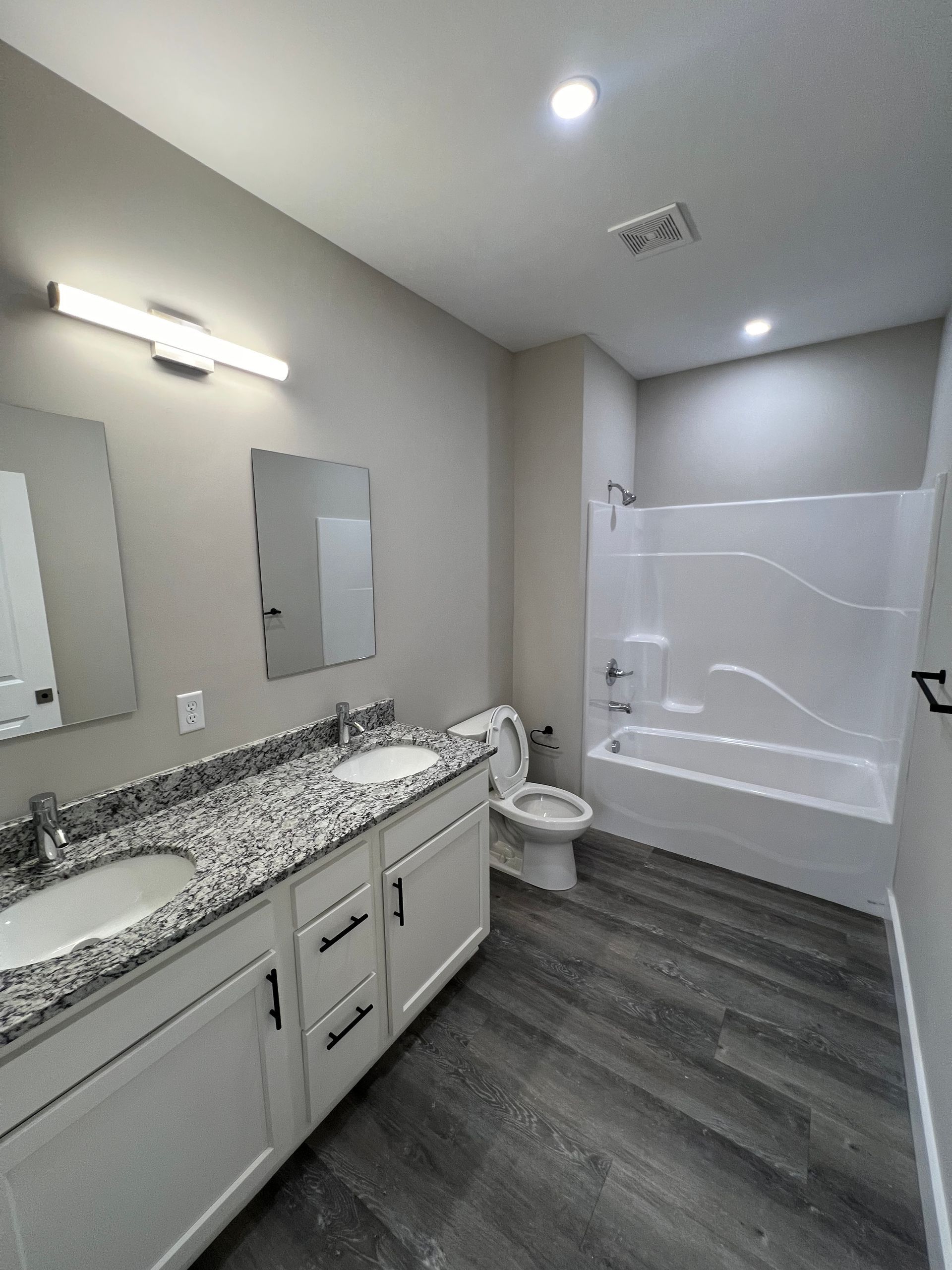 Bathroom with double vanity, bathtub, and toilet; gray and white color scheme.