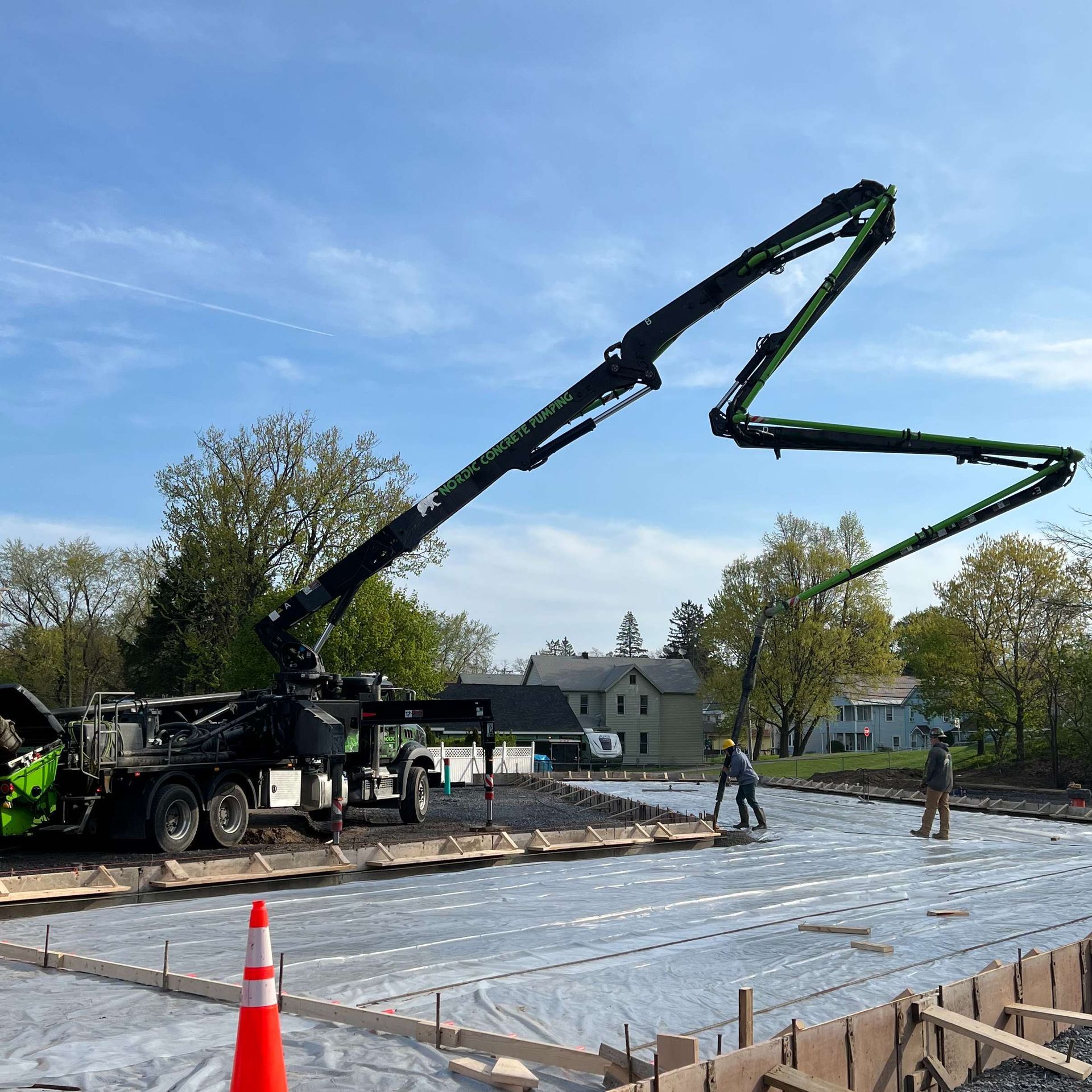 Concrete pump truck pouring concrete into a prepared foundation; workers nearby.
