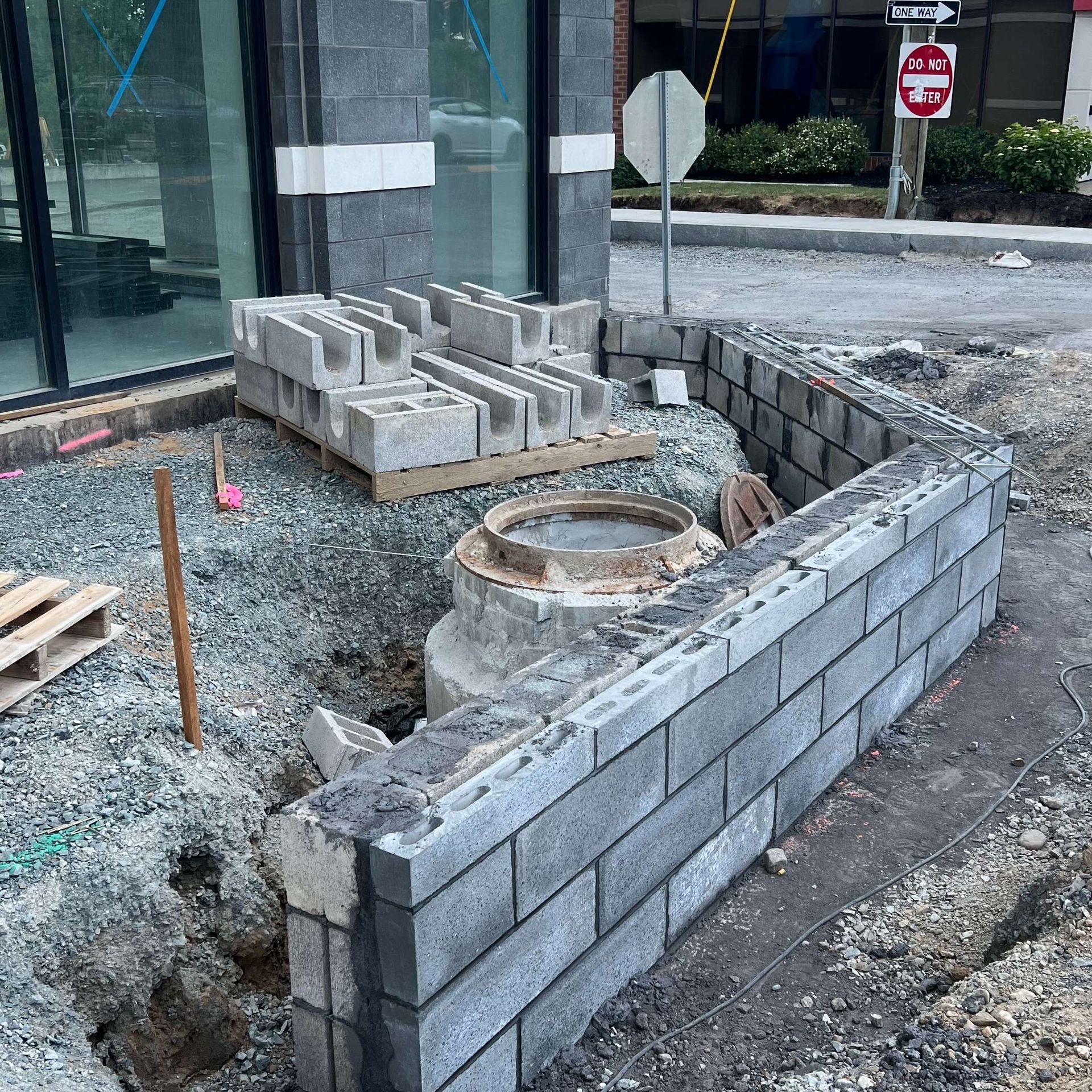 Construction site with cinder block retaining wall under construction. Gray blocks, gravel, and utility access.