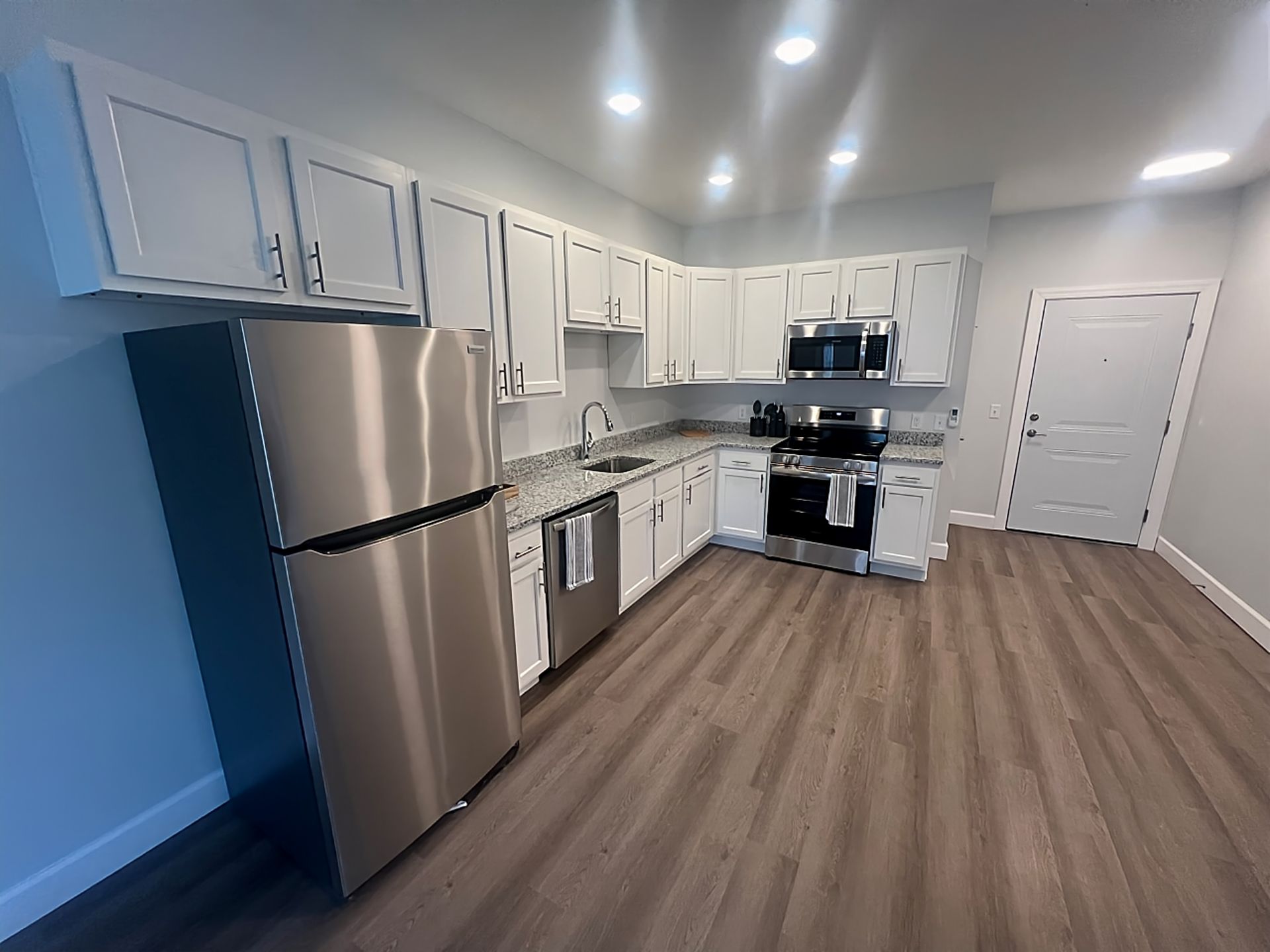 Kitchen with white cabinets, stainless steel appliances, and wood-look flooring.