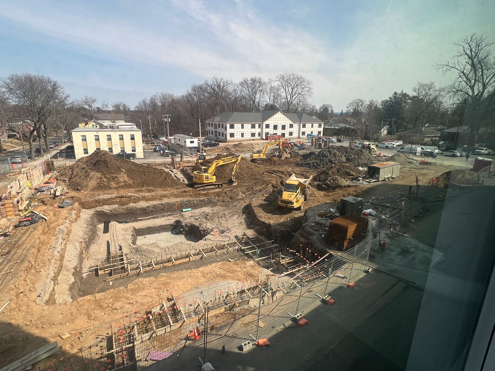 Construction site with excavators and earthmoving equipment, with buildings in the background.