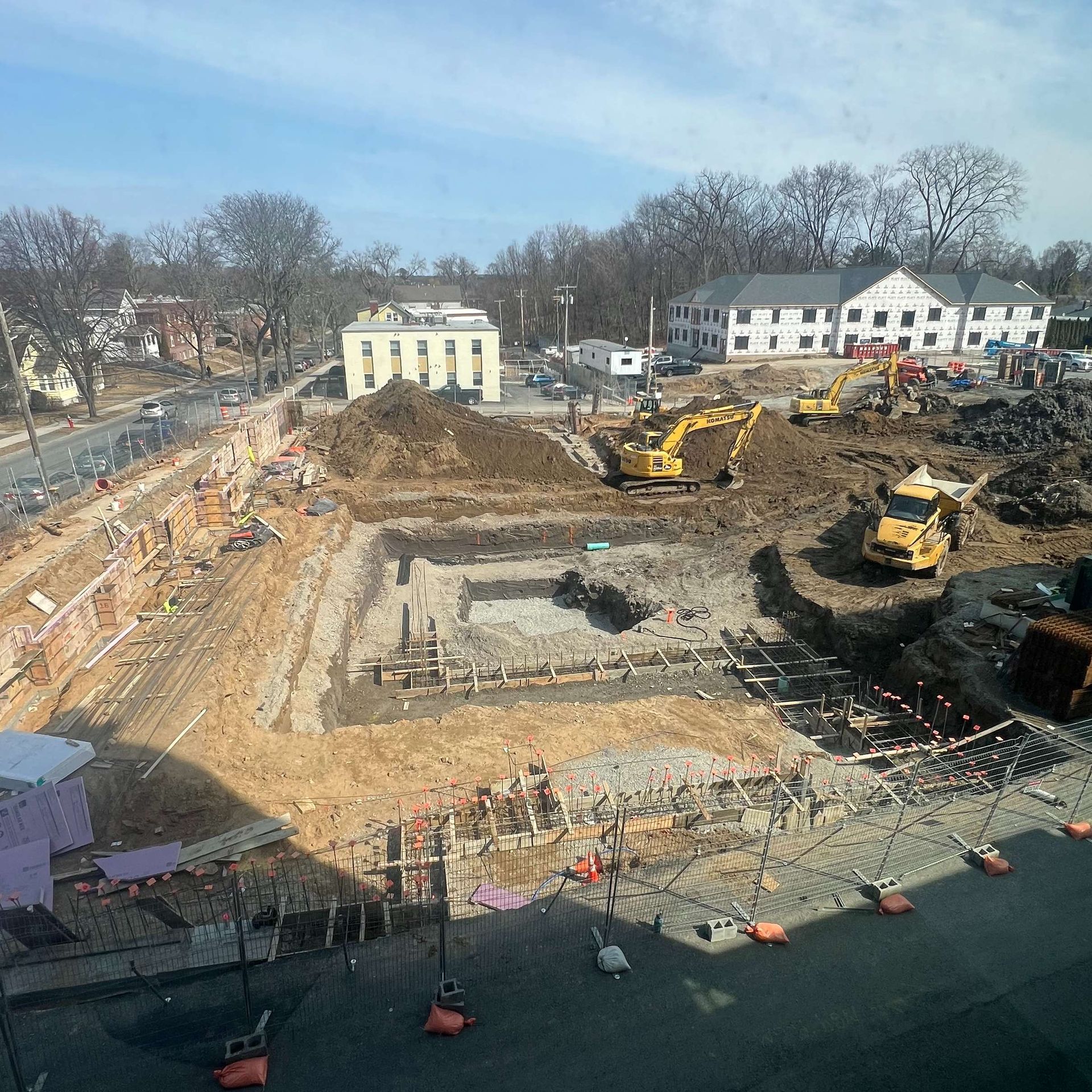 Construction site with excavators, a large pit, and surrounding buildings under a clear sky.