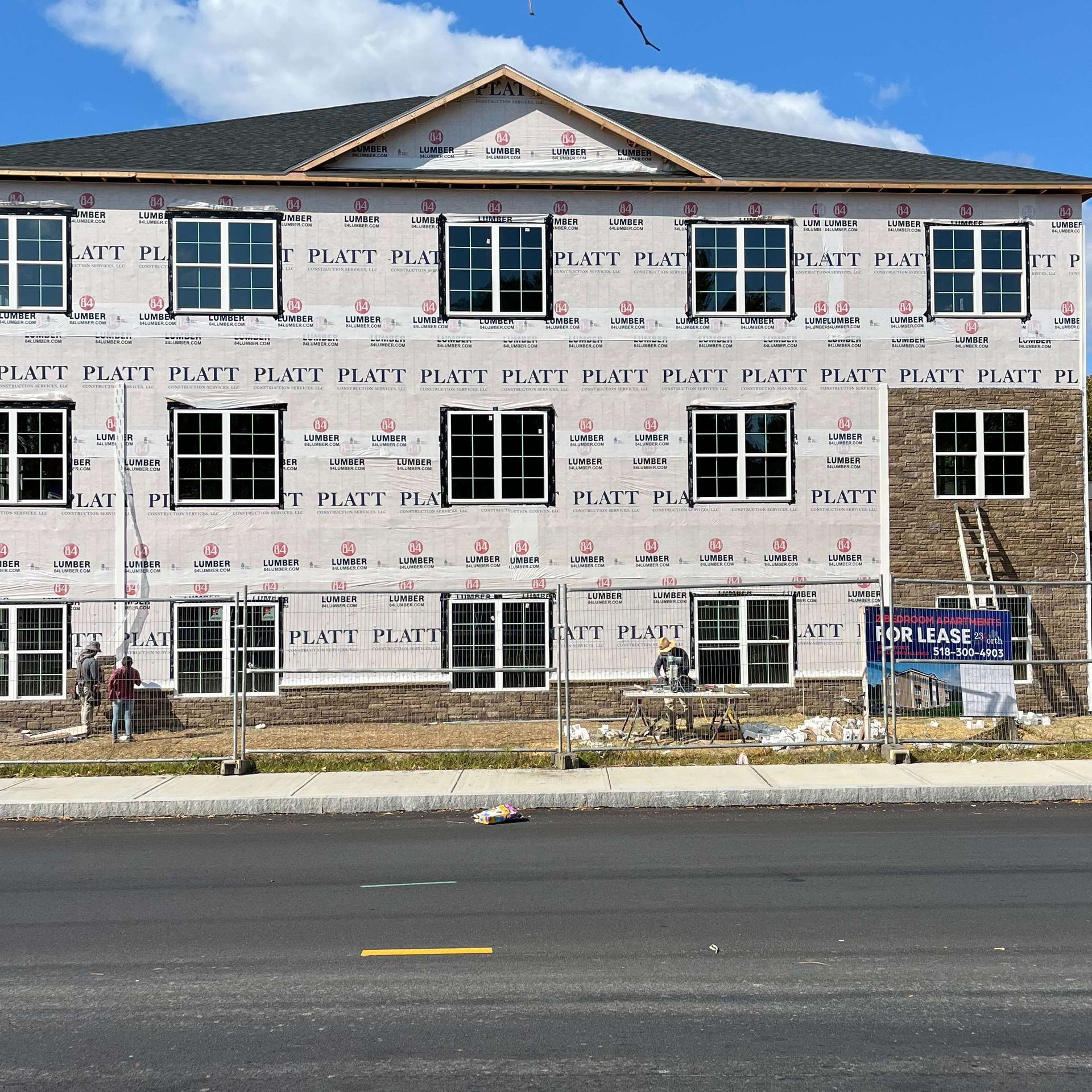 Multi-story building under construction; windows and protective wrap visible. Workers near the base.