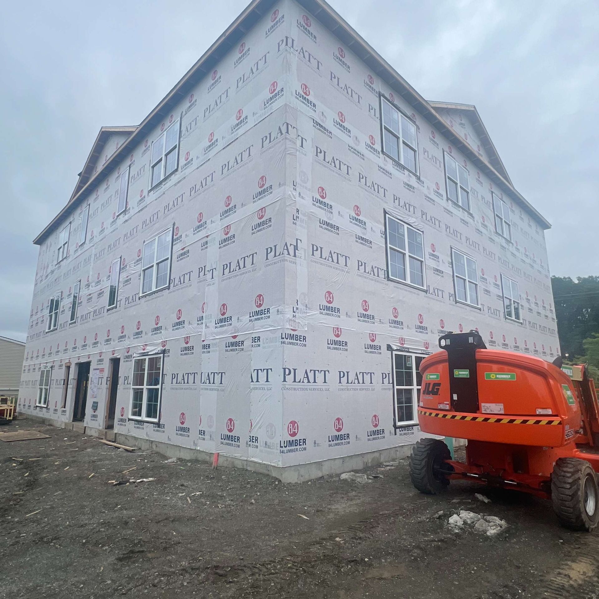 Building under construction with weather-resistant barrier and window installation. An orange lift is visible.