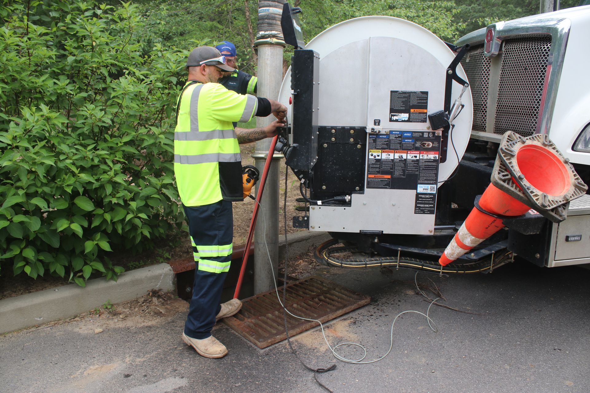 Worker in high-vis jacket operating a sewer vac truck hose beside a roadside drain chute