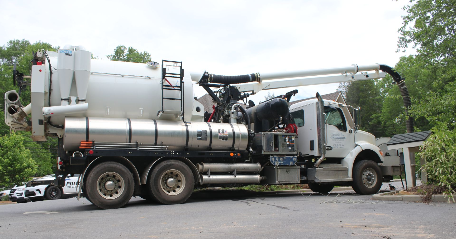 Large white industrial vacuum truck with hoses parked on a road among trees and cars. Hydro excavation. Hydro Escavation.