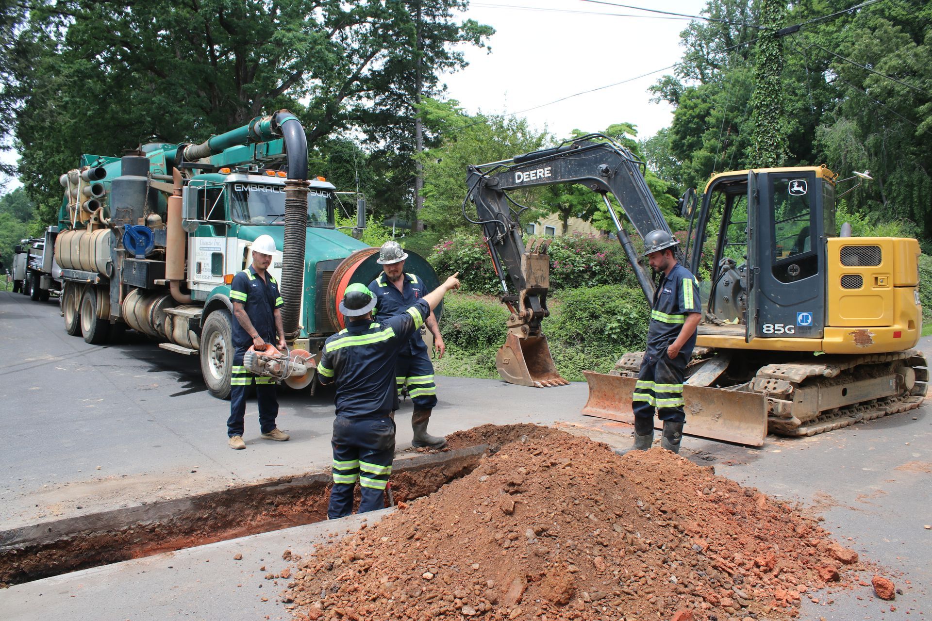 Workers use an excavator and truck to repair a road, with a pile of gravel in the foreground.