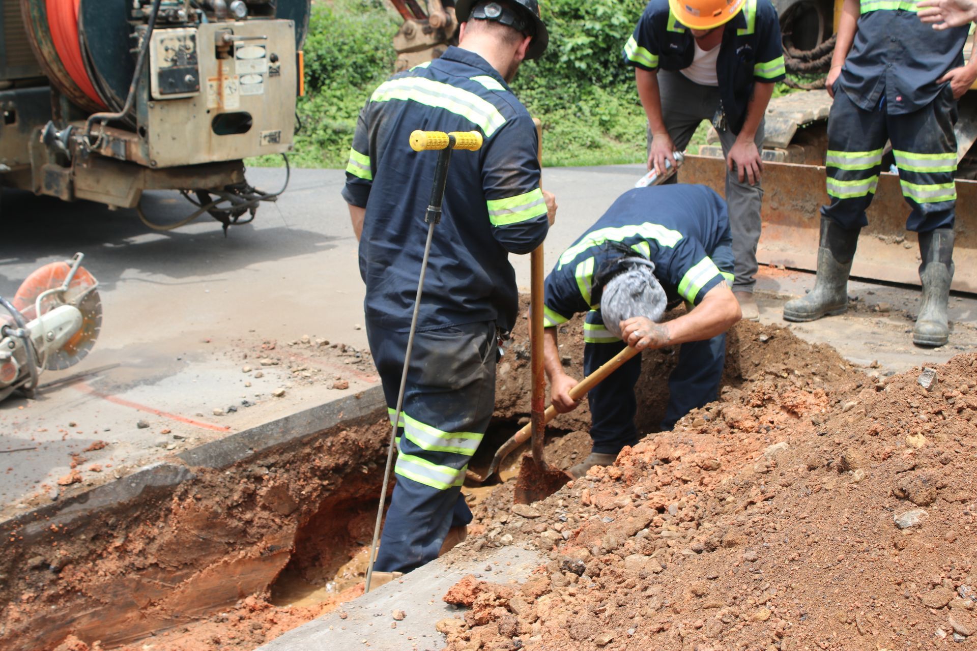 Workers in reflective gear repair a trench on a road beside a utility truck