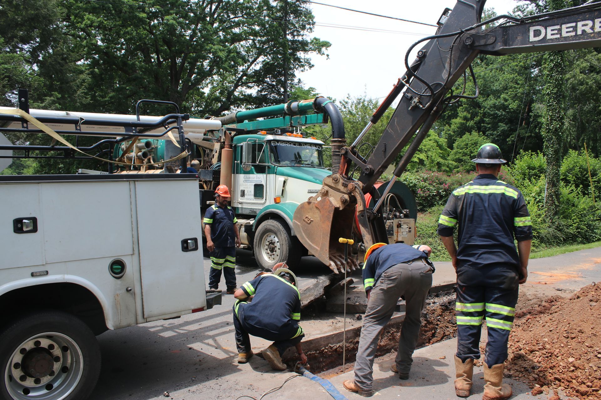 Utility crew repairing a roadside trench with excavator and truck on a tree-lined street