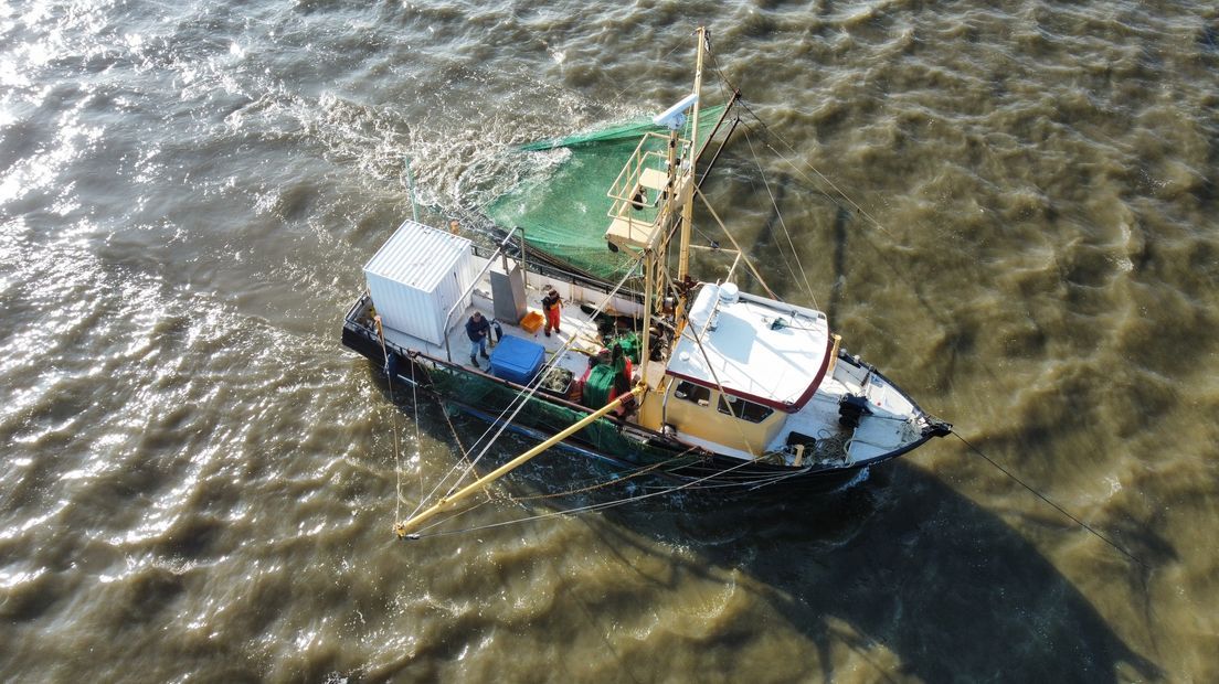 Fishing boat at sea with a green net deployed, people onboard.