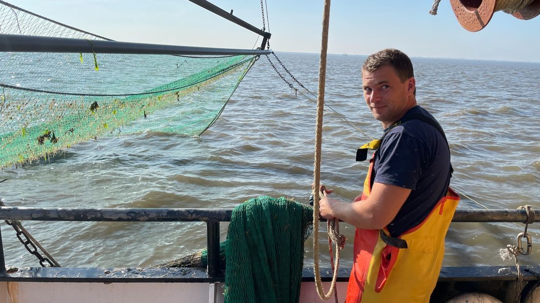 Man on a fishing boat pulling rope near a net; outdoors on a choppy sea.
