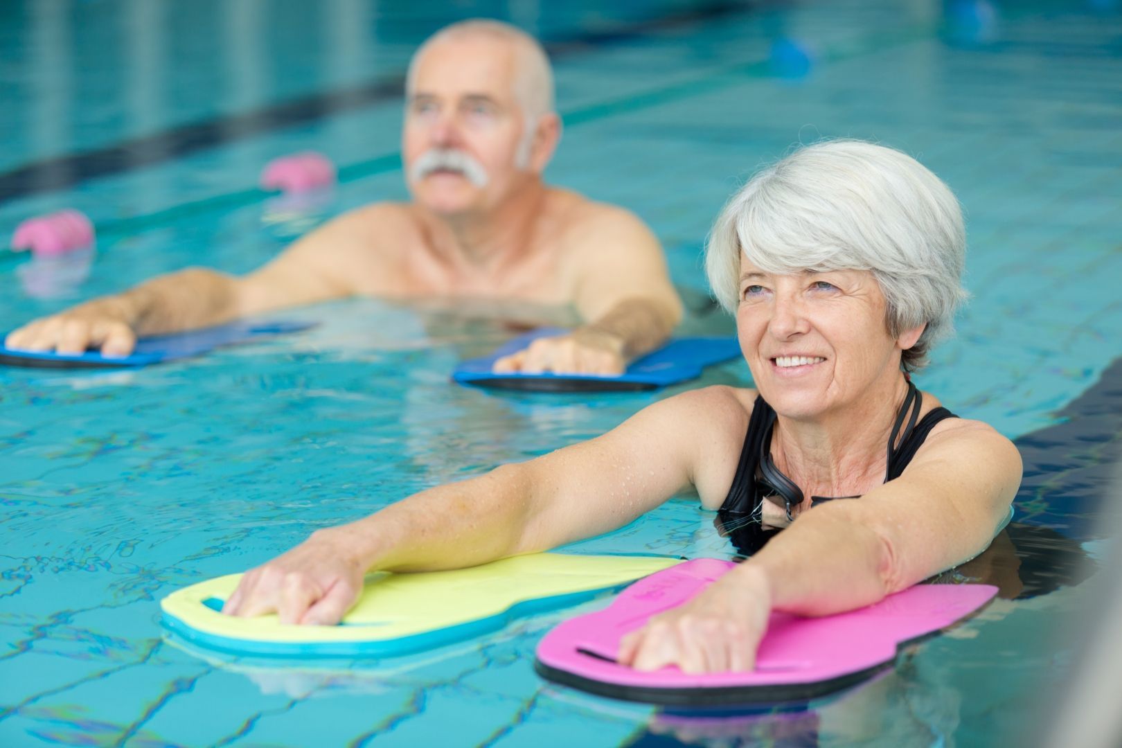 Two People in a Pool Doing Water Aerobics With Flotation Boards — PhysioCare Townsville in Deeragun, QLD