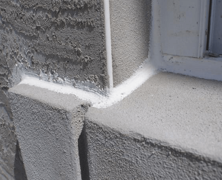 White stucco corner detail beside a window frame and trim on a building facade