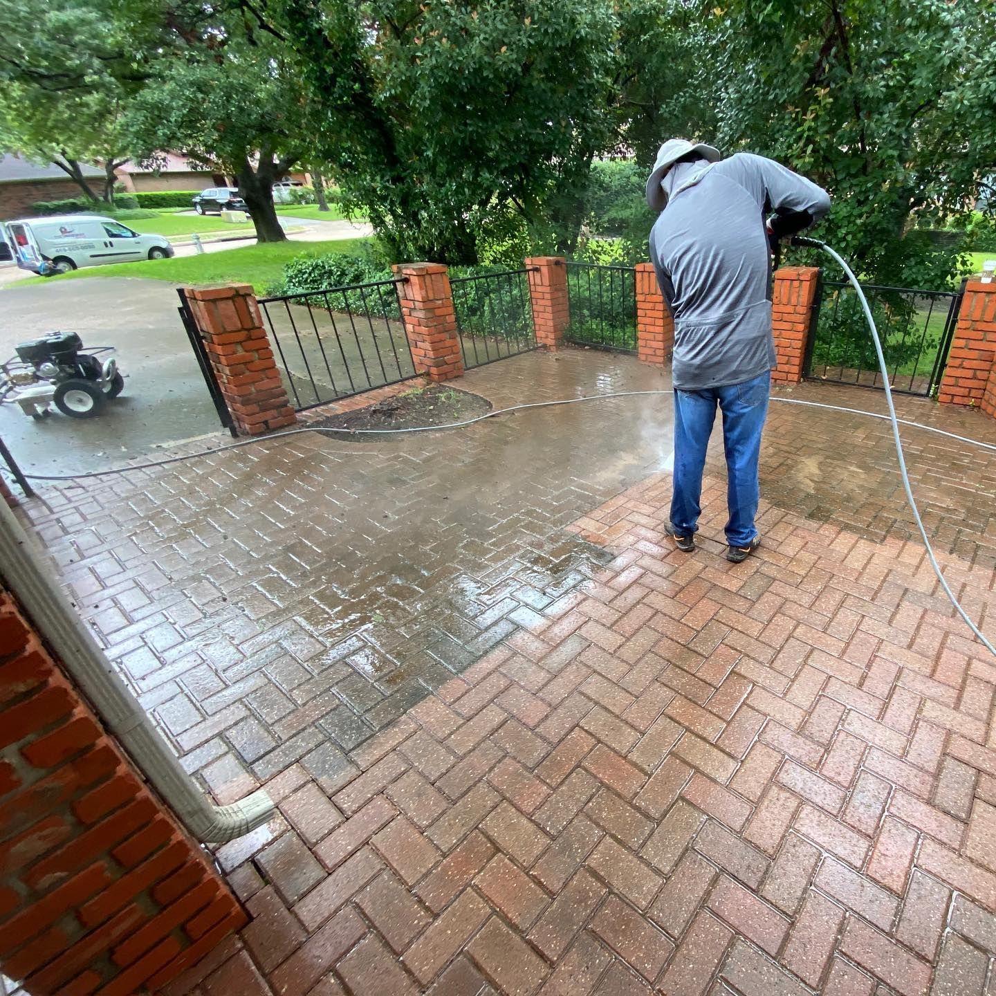Person pressure-washing a wet brick porch beside a brick railing and green yard