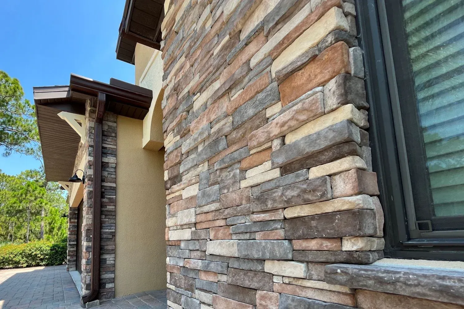 Stone exterior wall and window of a house with a covered entry and blue sky