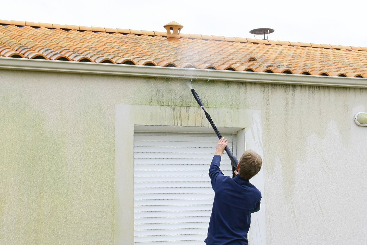 Person using a long brush to clean a house wall under a tiled roof