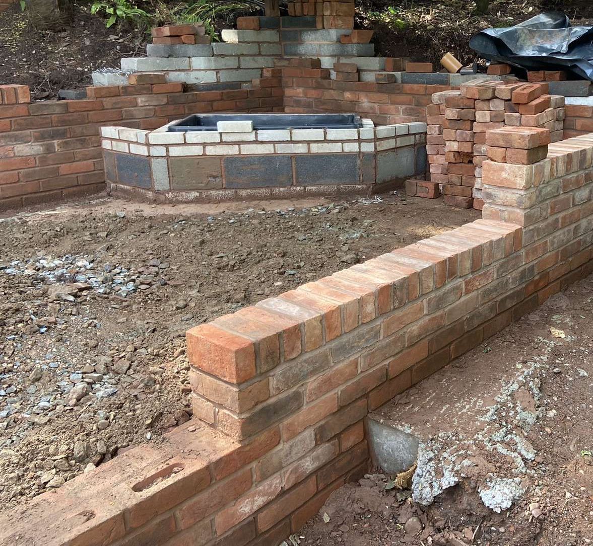 Brads Stunning Garden Wall Brickwork under construction in a garden: a tiered structure, fire pit, and retaining wall.