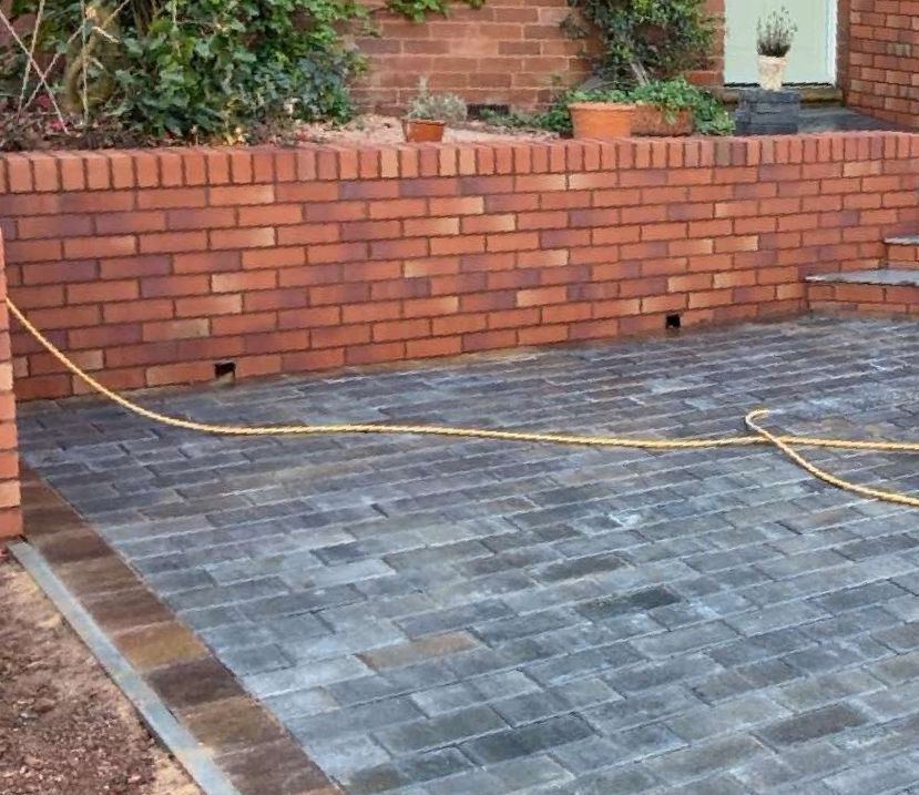 Brads Stunning brick Wall brick wall with pathing in driveway with sand on floor and bushes in background