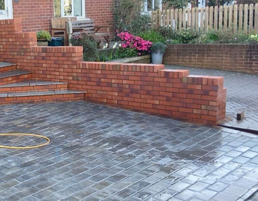 a brick wall built next to a new pathing driveway cleaned and new