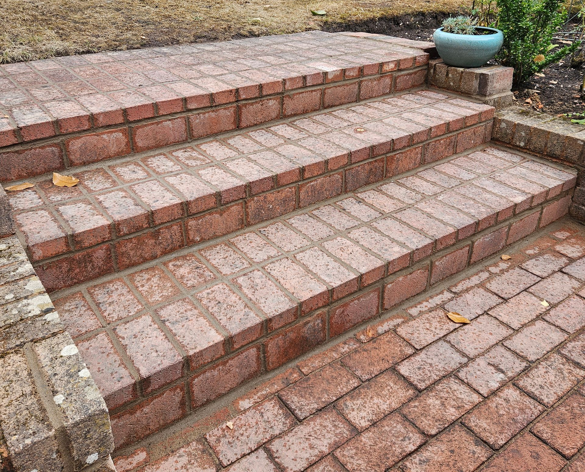Brick steps leading to a raised area, constructed of red bricks. A potted plant is nearby.