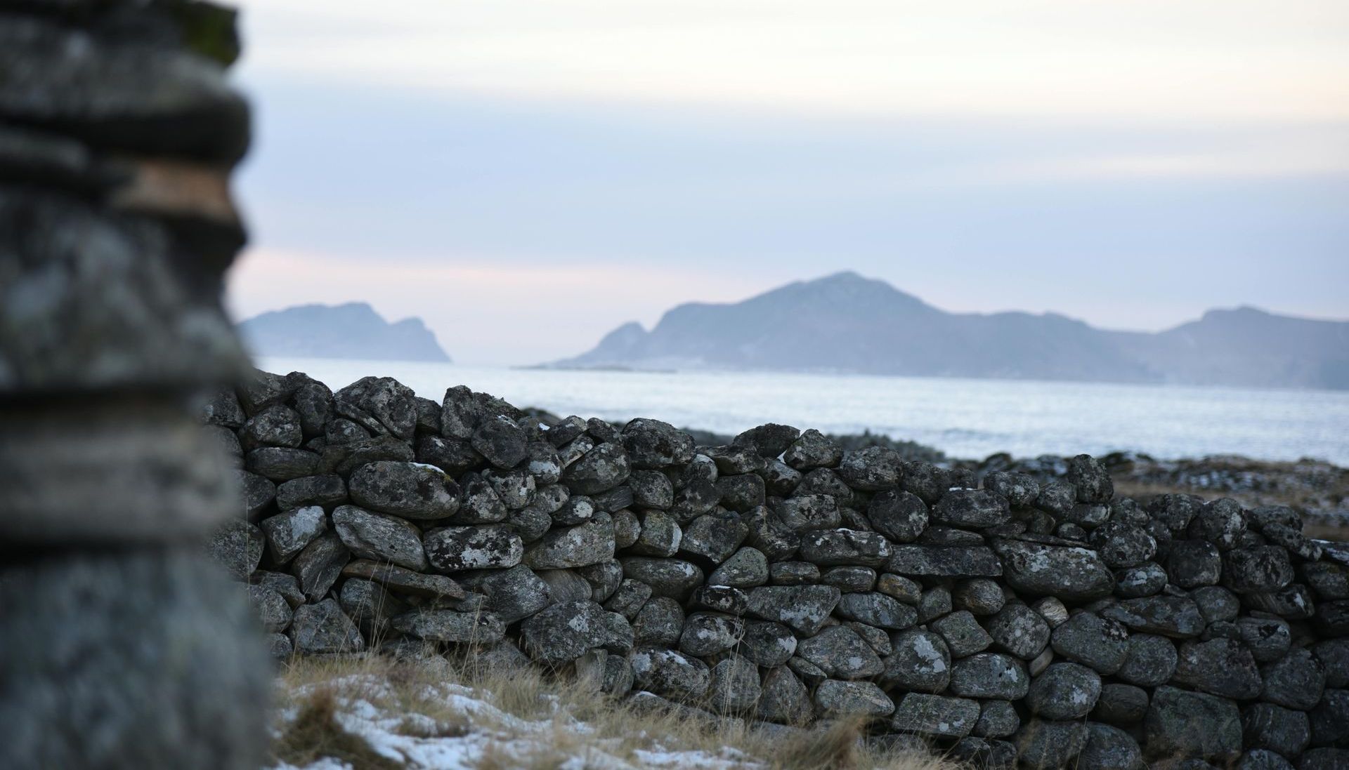 A stone wall with a view of the ocean and mountains in the background.