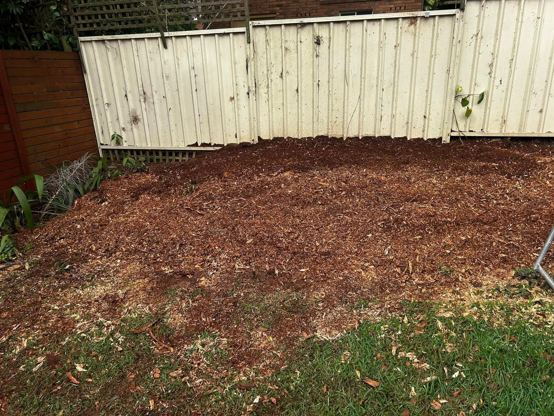 A White Fence is Sitting Next to a Pile of Wood Chips in a Backyard — All One Arb Tree Service In Bonny Hills, NSW