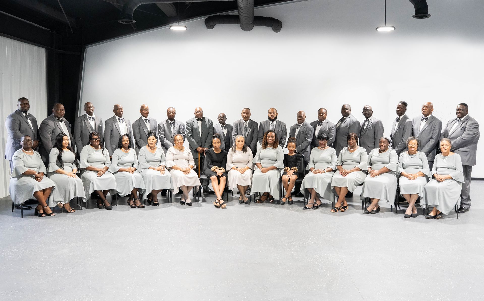Formal group portrait of people in gray and white attire standing and seated in a studio setting