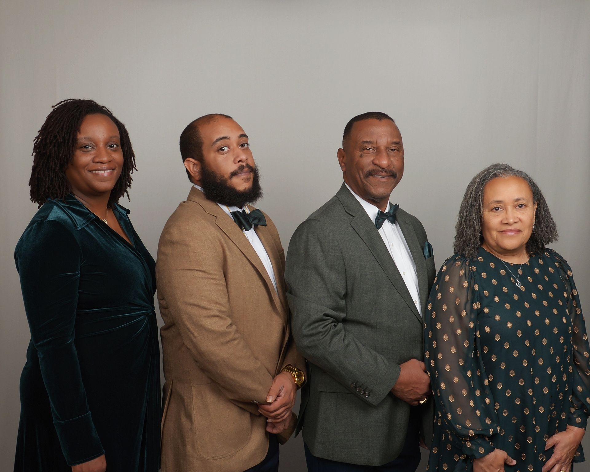 Four people pose together in formal attire against a plain backdrop.