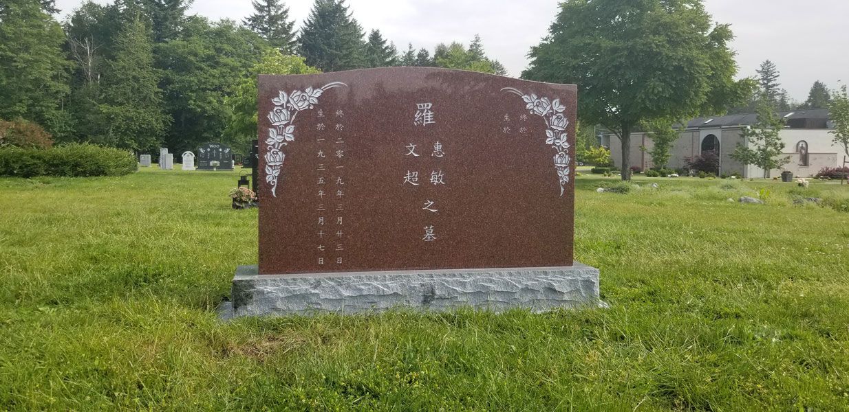 A red gravestone is sitting in the middle of a grassy field.