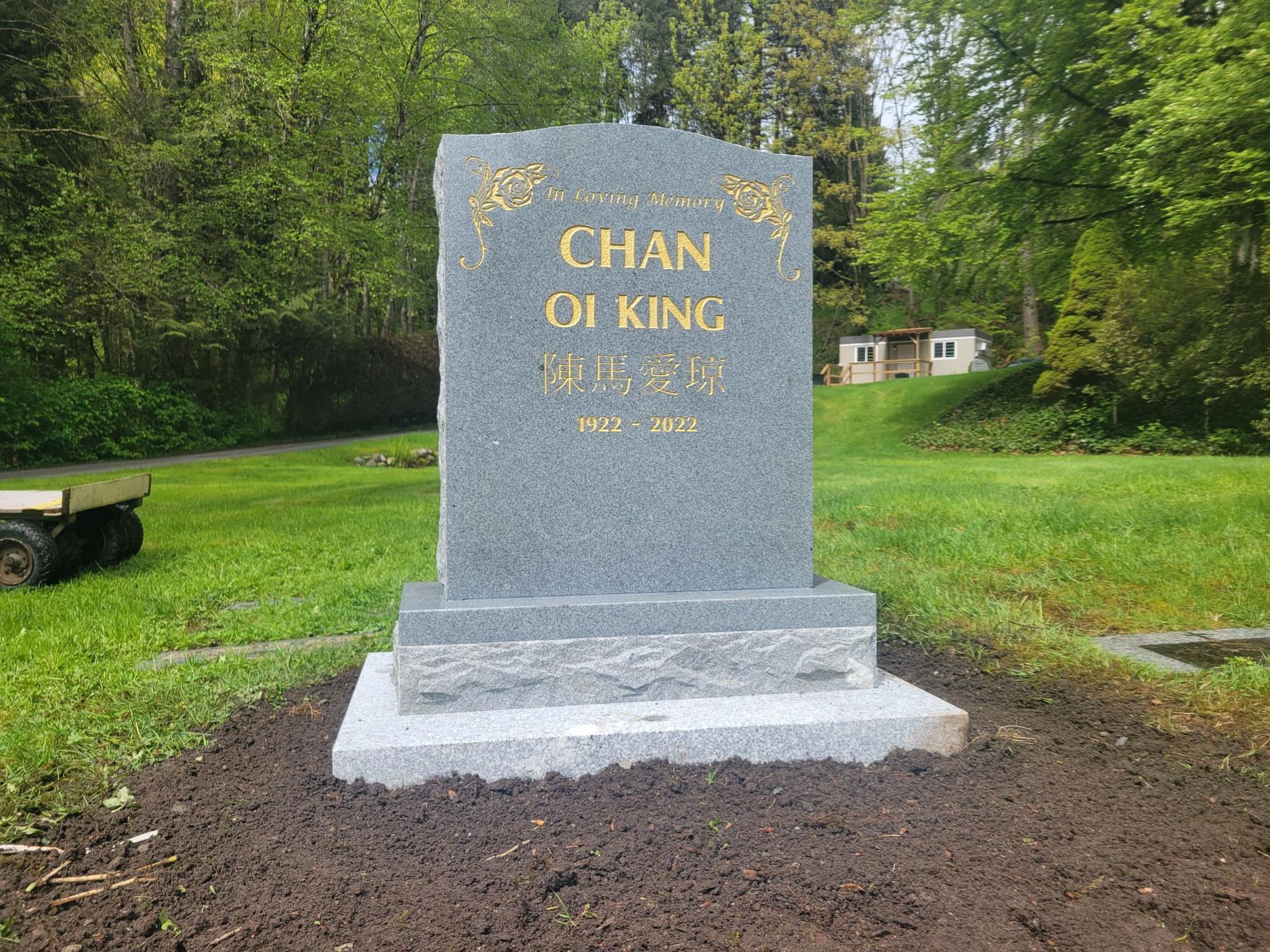 a gravestone for chan oi king is sitting in the middle of a grassy field .