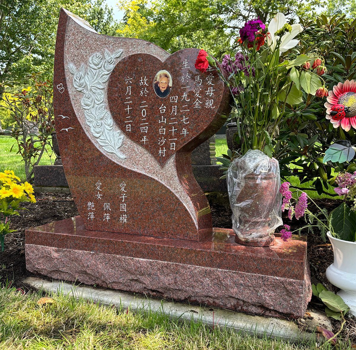 Custom heart shape upright headstone with carved roses and a photo plaque and matching granite vase. Made of pacific red granite.