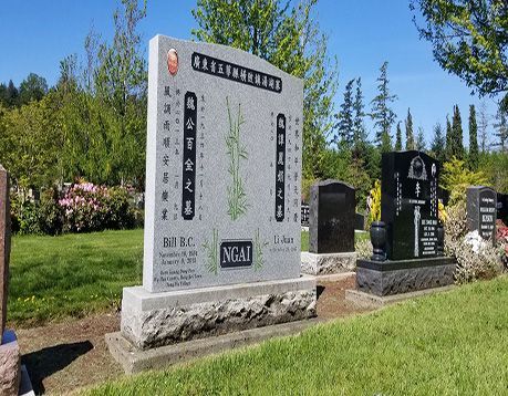A large stone monument in a cemetery with chinese writing on it.