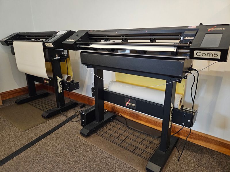 Two coms printers are sitting next to each other in a room.