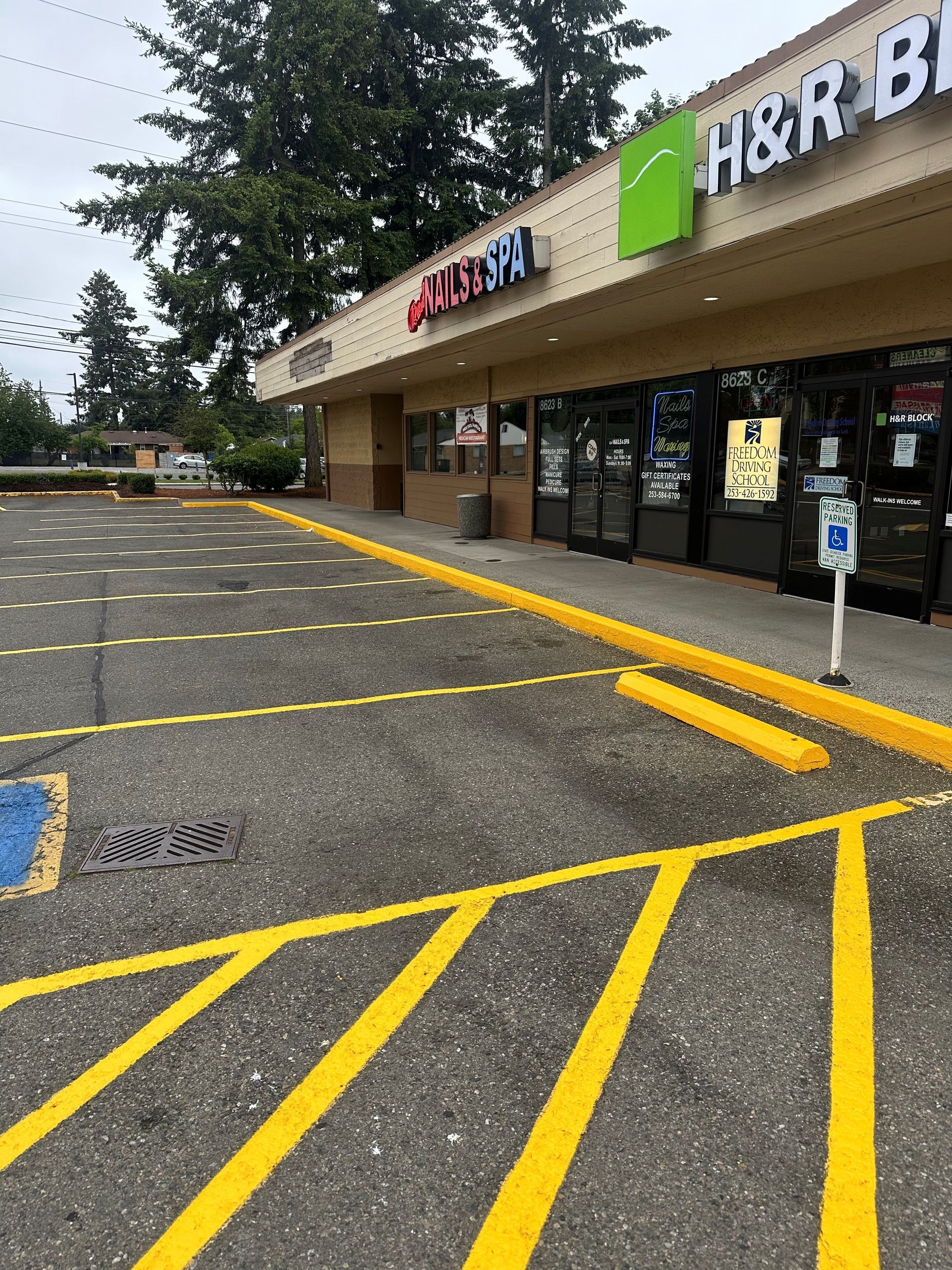 A silver car with a damaged bumper is parked in a parking lot