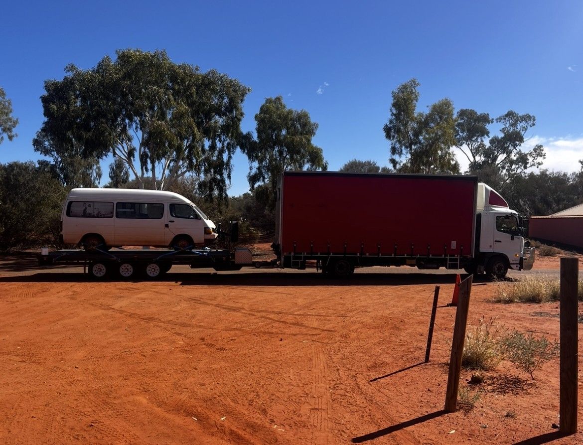 Red semi-truck parked beside a highway, green and yellow fields in background, blue sky with clouds. — Red Centre Transport in Braitling, NT