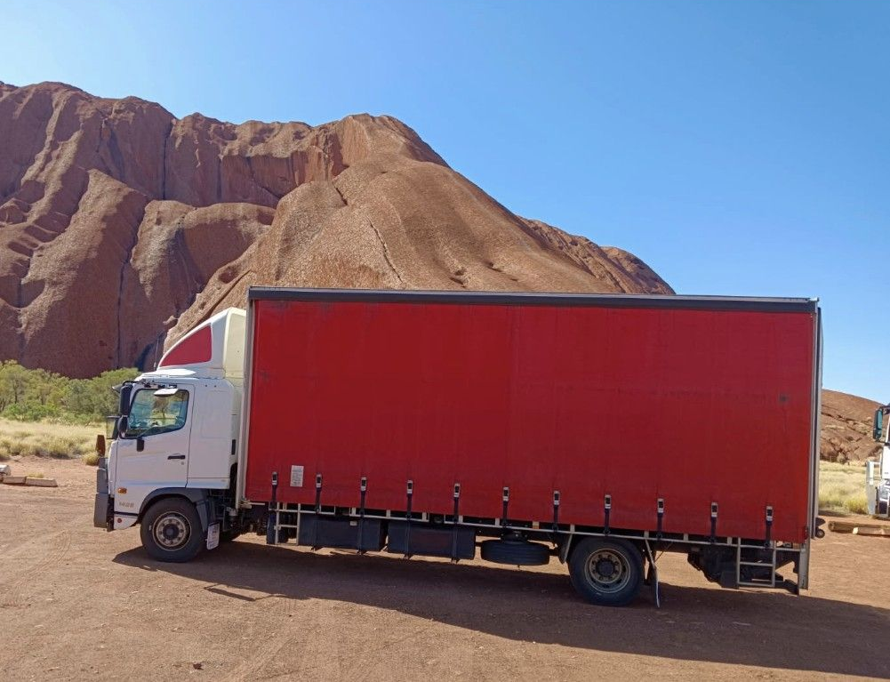 Semi-truck driving on a road at sunset, with a bright sky in the background. — Red Centre Transport in Braitling, NT