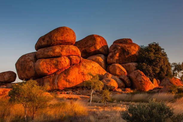 Sunlit orange boulders stacked in a desert landscape under a clear blue sky