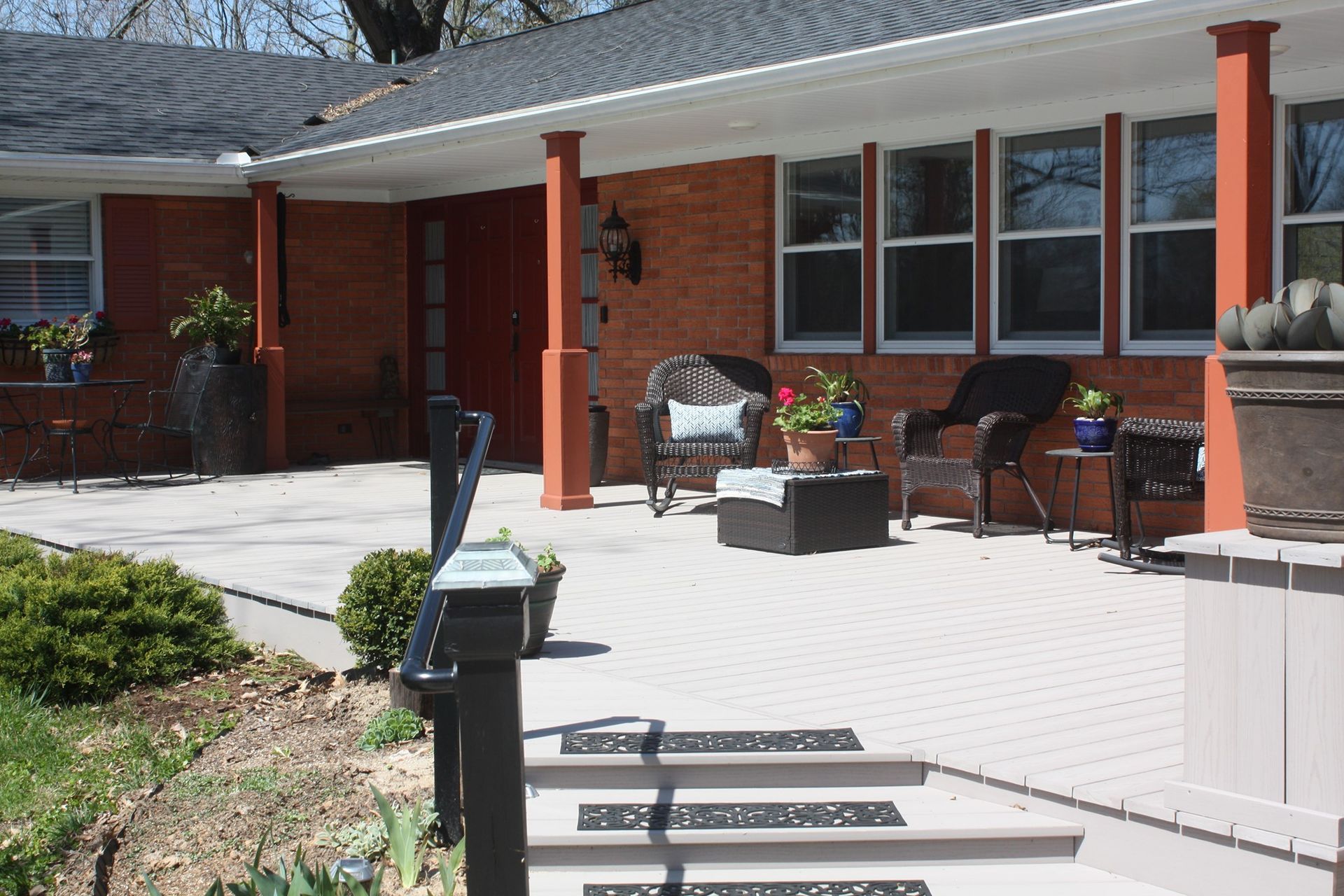 Brick house front porch with white steps, red columns, and potted flowers in sunlight