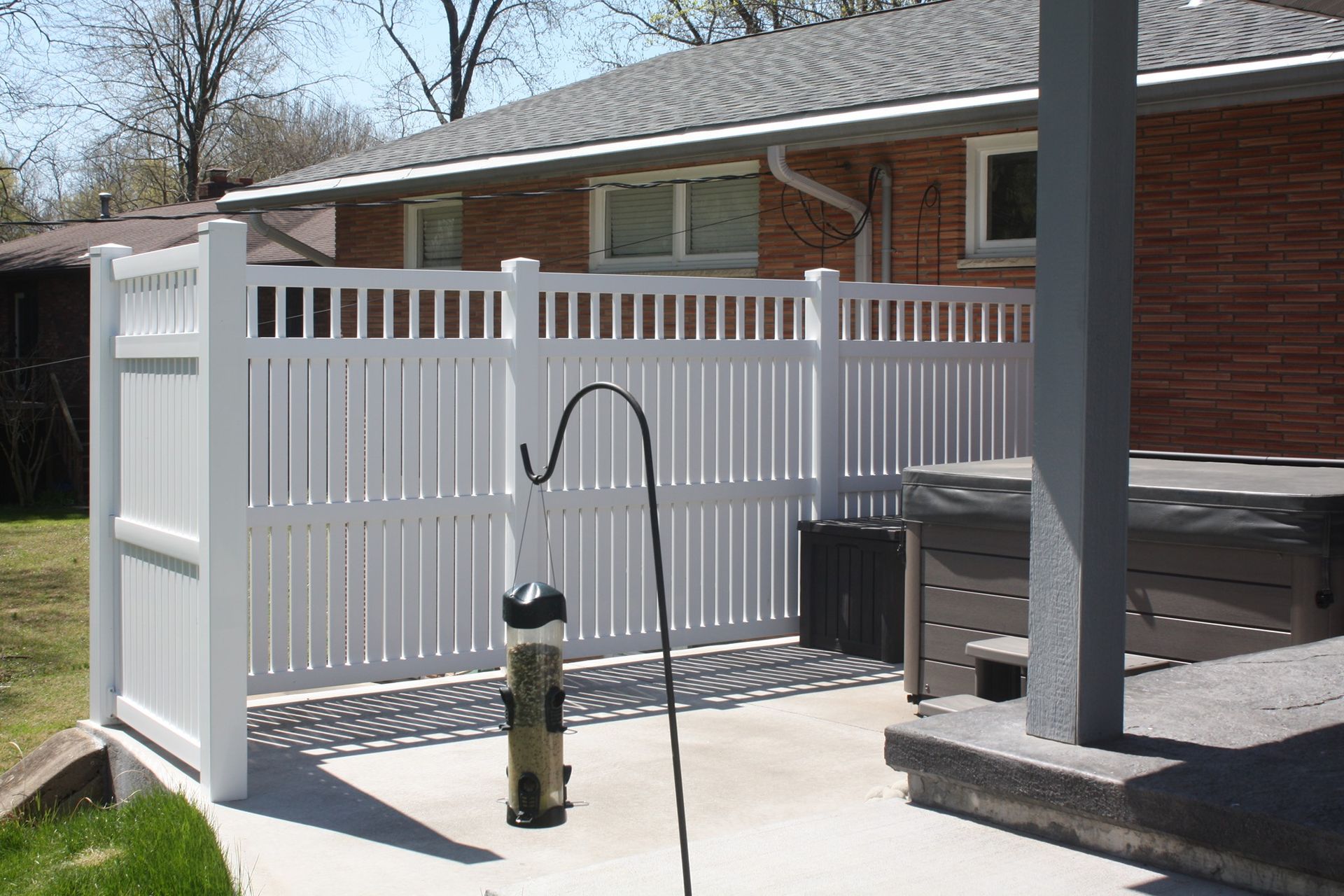 Backyard patio with a fenced-in hot tub and bird feeder beside a brick house