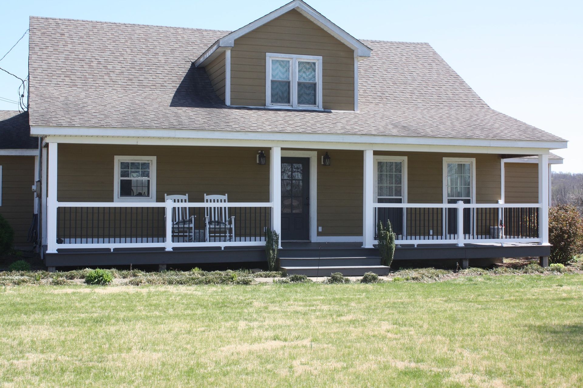 Brown house with white trim and a covered front porch on a grassy lawn