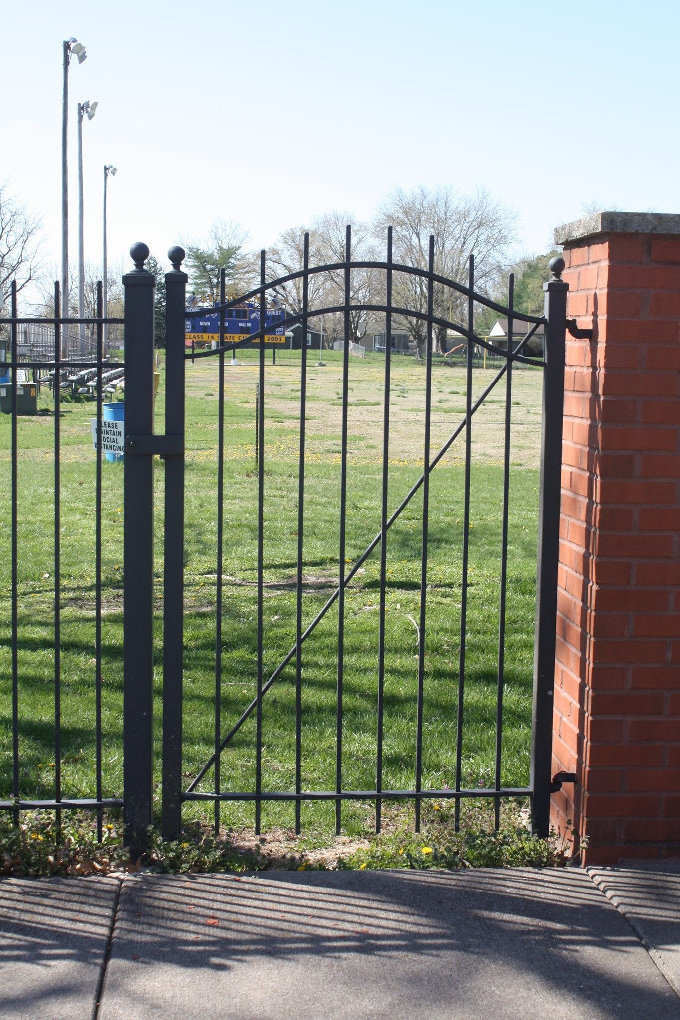 Black metal gate beside a brick pillar, opening onto a grassy field under a clear sky