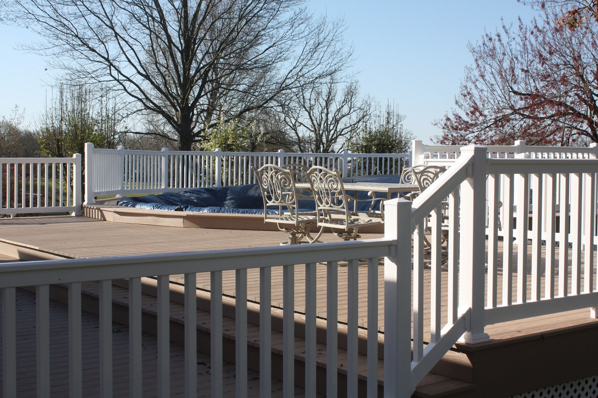 White deck with railings and chairs, overlooking leafless trees on a sunny day