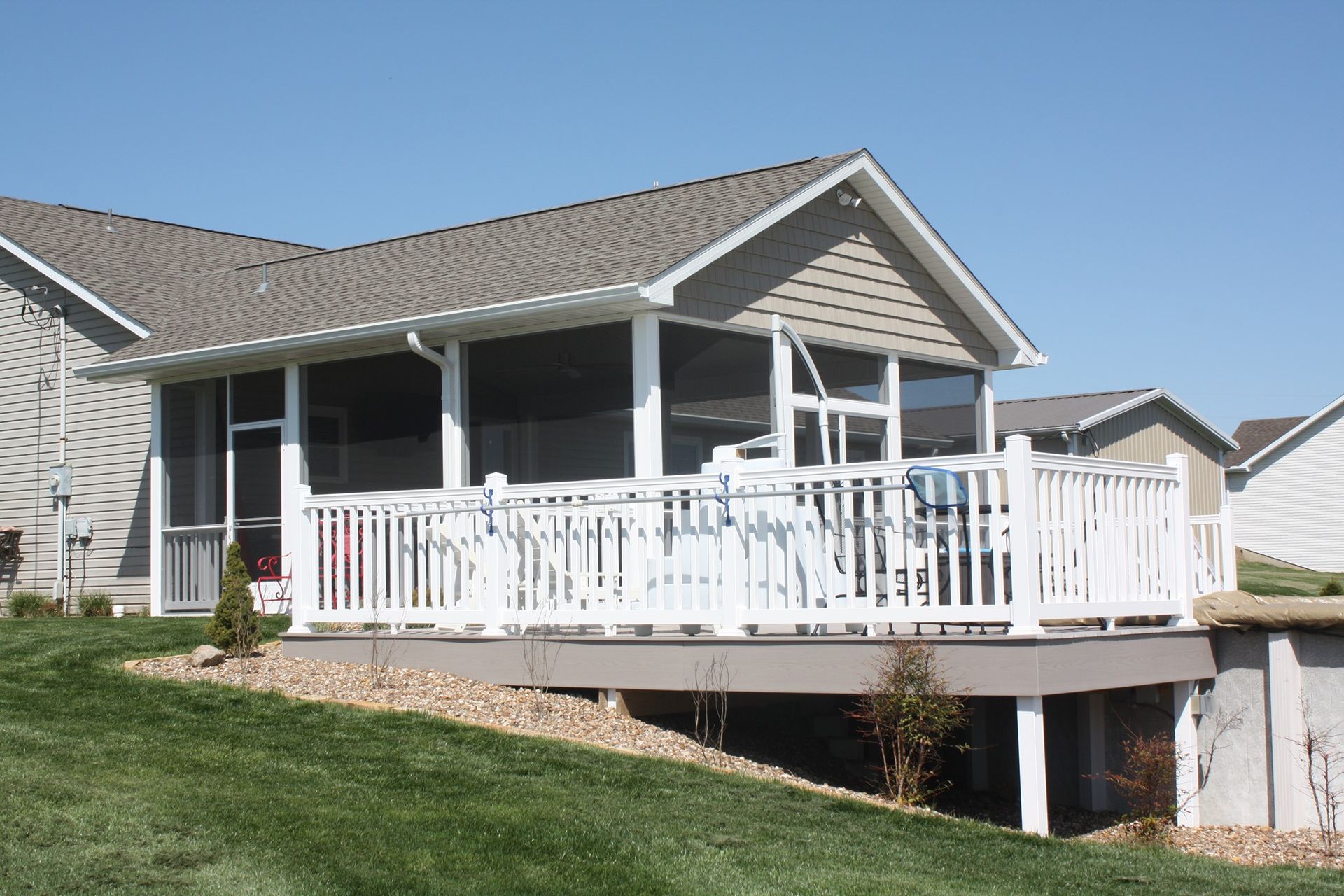 Suburban house with white-railed porch and screened patio on a sloped lawn