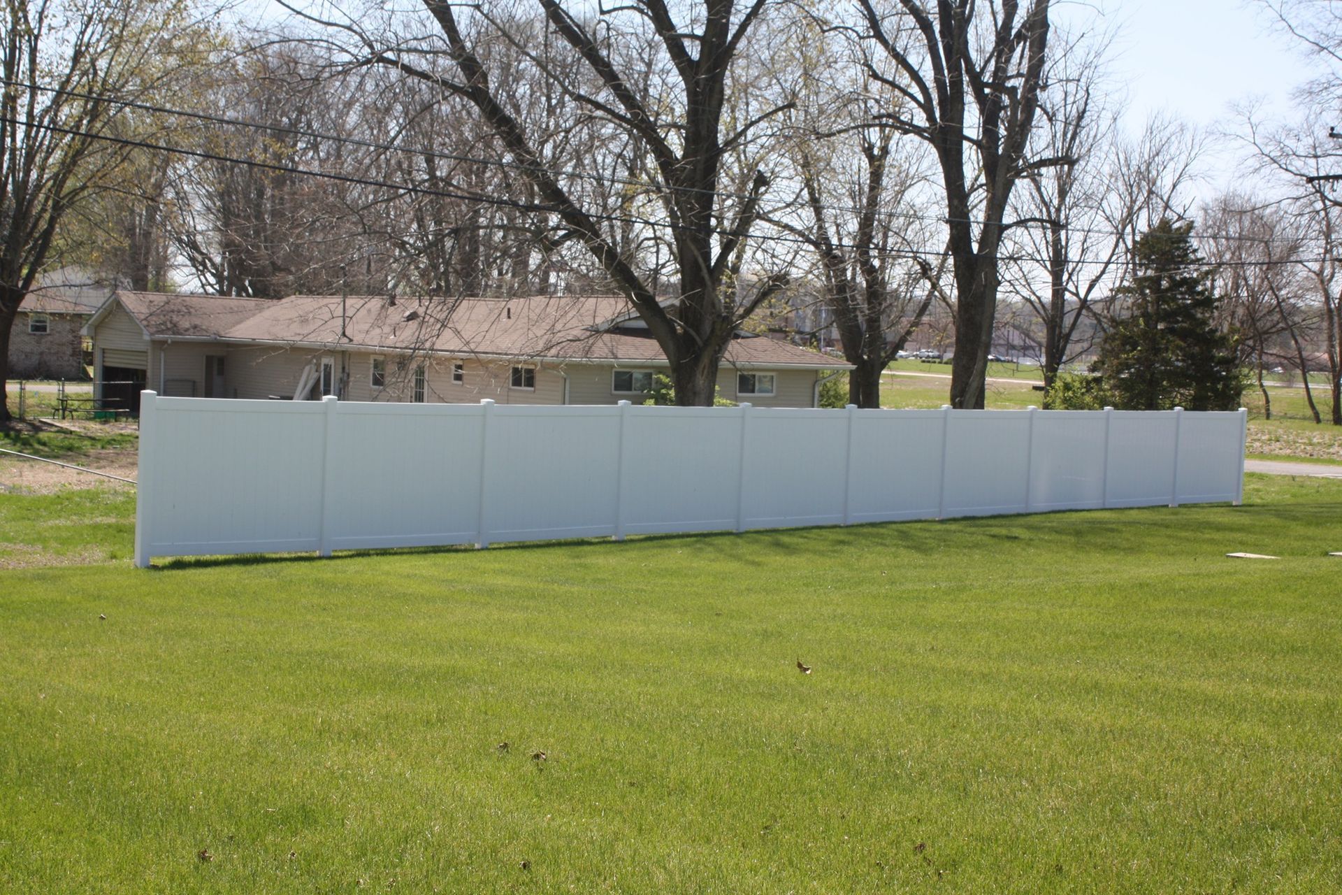 White fence panels across a grassy yard with bare trees and a house in the background