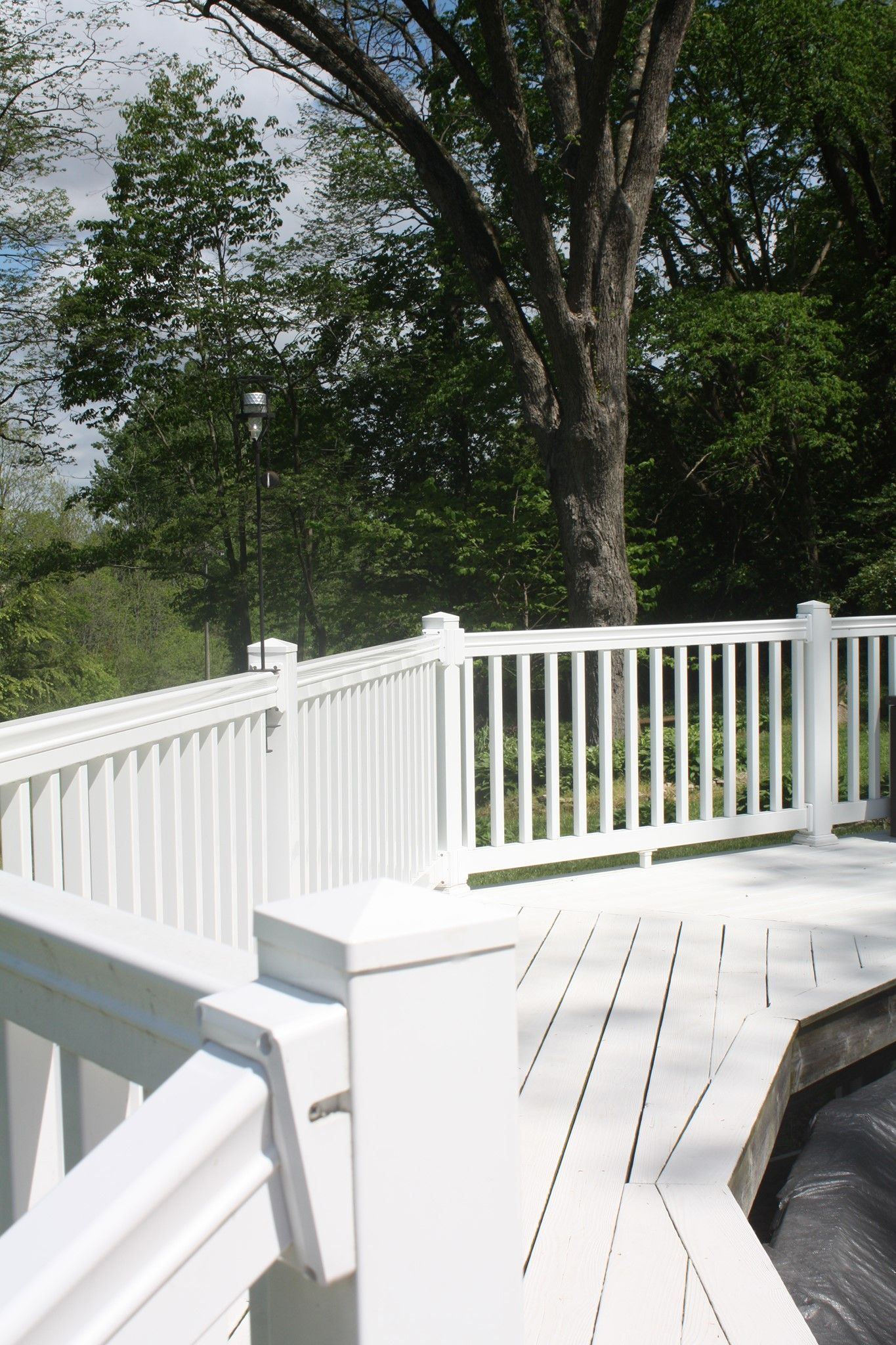 White wooden deck with railing beside trees and greenery on a sunny day