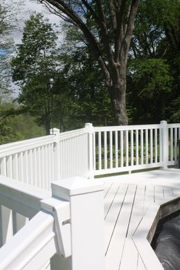 White wooden deck with railing overlooking green trees on a sunny day