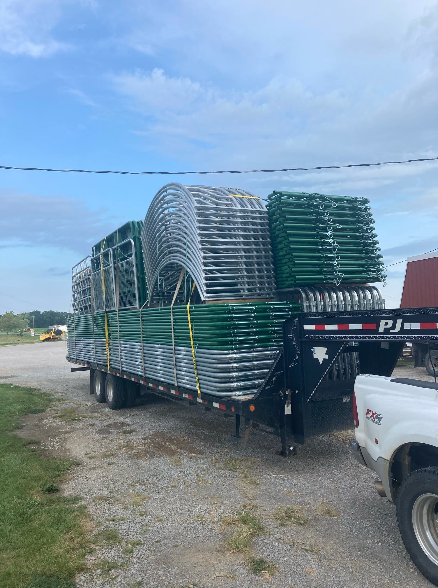 Flatbed trailer loaded with stacked green and silver metal chairs in a gravel lot under a blue sky