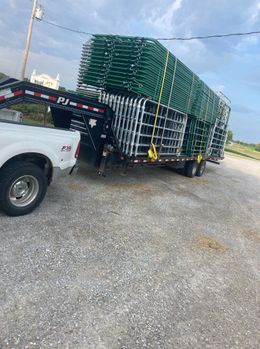 White pickup towing a black flatbed trailer stacked with green panels on a gravel lot.