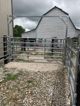 Gravel farm lane leading to a metal gate and white barn under a cloudy sky
